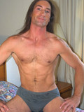 Sporty long haired brunet gay strips nude and shows it all in the middle of a bed