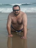 fat-hairy-chested-bear-in-shades-poses-nude-in-wet-sand-on-the-wild-beach